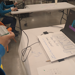 A laptop running PWOP has the keyboard covered with a hand-drawn PWOP sign. It's connected to a phone-sized box with 18 translucent plastic bubbles on top reminiscent of bubble wrap.